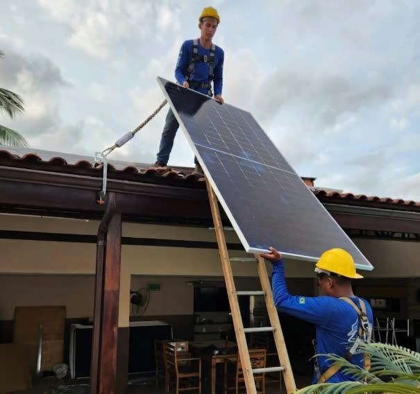 Instaladores da ASG Energia, com capacete e cinto de segurança, posicionando placa solar