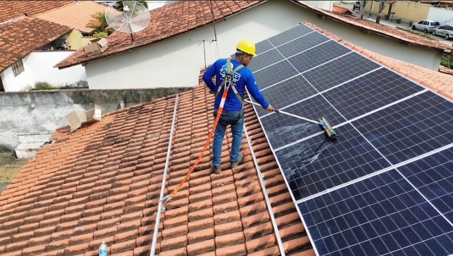 Instalador da ASG Energia, com capacete e cinto de segurança, limpando painéis solares